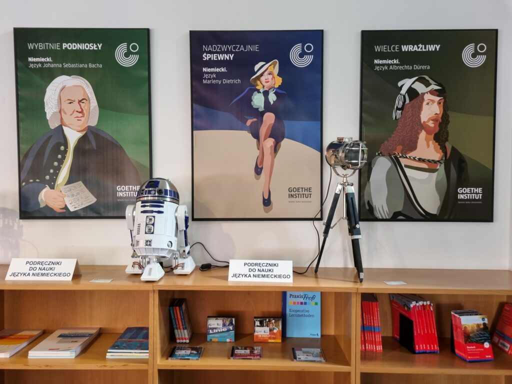 Framed posters with representatives of German art (Jan Sebastian Bach, Marlena Dietrich, Albrecht Dürer) and a bookshelf with books, including German language textbooks.
